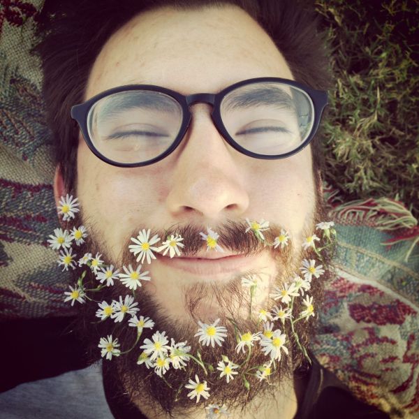 Foto graciosa de un hipster feliz con margaritas en la barba larga