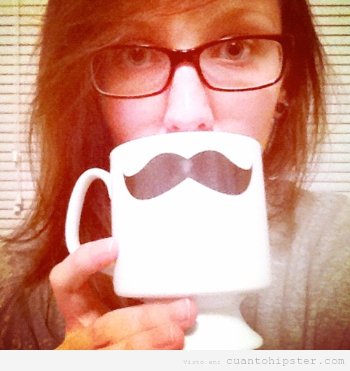 Chica hipster con taza de cabé con un bigote hipster dibujado