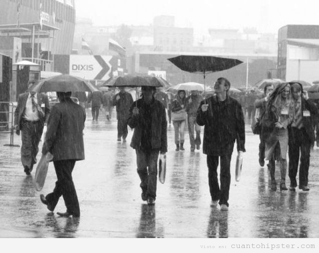 Foto de un hombre hipster caminando bajo la lluvia con el paraguas al revés