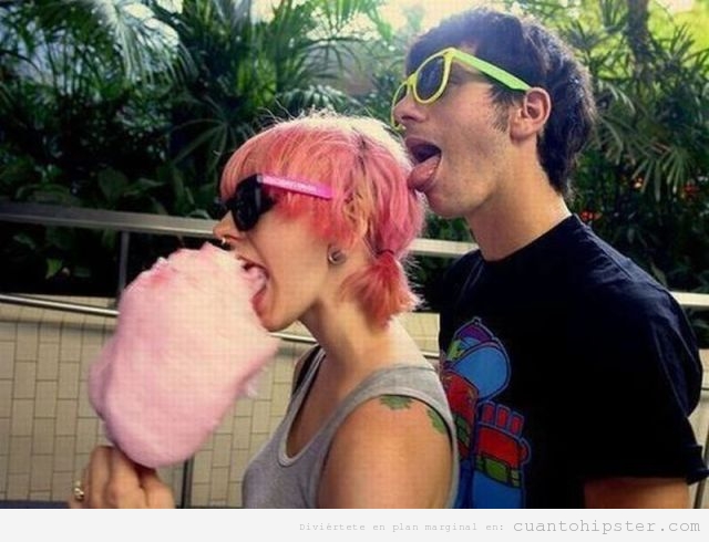 Pareja hipster, chica comiendo algodón de azucar y chico chupando su pelo rosa teñido