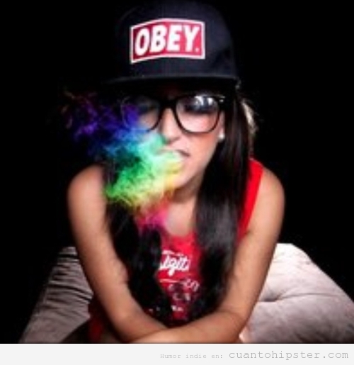 Chica hipster con gorra de camionero y gafas de pasta fumando humo de colores