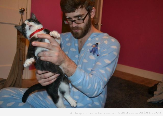 Chico hipster con pijama de cuerpo entero, gafas de pasta y gato