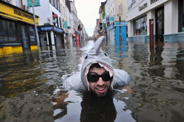 Moderno con disfraz de tiburón en una calle inundada